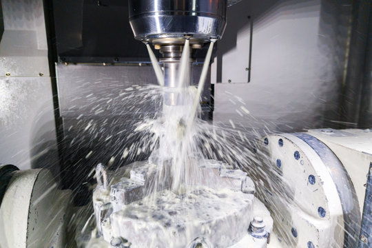 a process of industrial wet milling in 5-axis cnc machine with coolant flow under pressure and motion blur of splashes