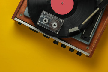 Retro music concept. Vinyl record player with a vinyl record, audio cassette on yellow background. 80s. Top view
