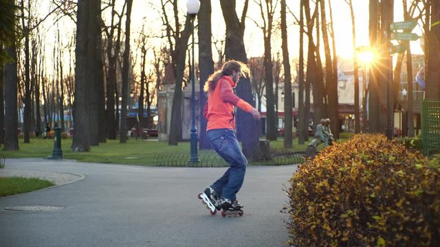 Cool bearded man skates and dances on roller skates in autumn in a central city park on a background of trees. Active sports and healthy lifestyle. Side view in slow motion.