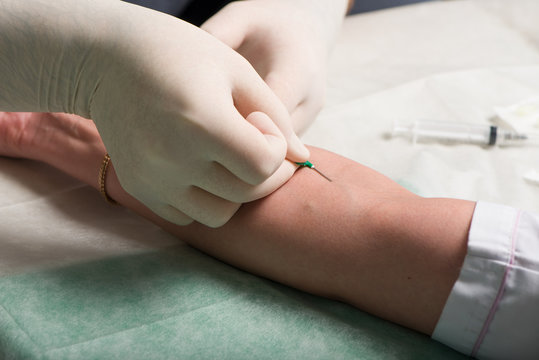 Hands in latex medical gloves perform vein puncture in area of ulnar bend of patient 's hand