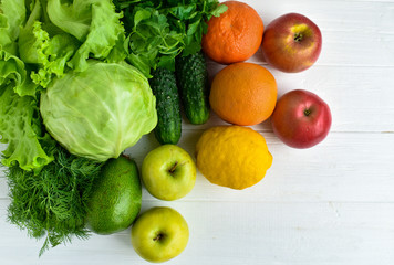 Green cabbage, parsley, cucumbers, salad, avocado, apple, orange orange, mandarin, yellow lemon, red apples on a white wooden background. Healthy eating concept.
