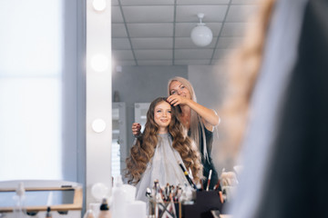 Make-up artist and model look in the mirror and sit up the hairstyle, festive image in the beauty salon