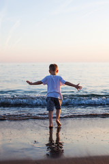 A little boy runs along a sandy beach in the sea at sunset