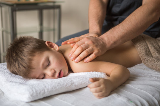 Boy toddler relaxes from a therapeutic massage. Physiotherapist working with patient in clinic to the back of a child