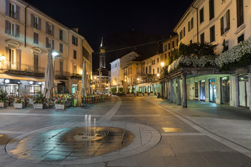 Downtown deserted city street scene at night. Lecco, Italy. Picturesque town overlooking lake Como. Square XX Settembre near the old Viscontea tower - obrazy, fototapety, plakaty