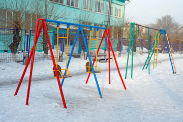 Fototapeta na wymiar Children's swing on the playground in the ordinary courtyard of an apartment building. Russia. Winter