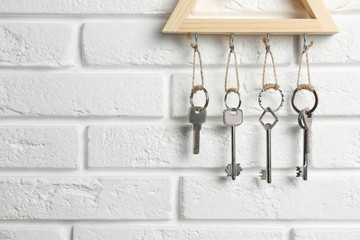 Wooden key holder on white brick wall indoors, closeup. Space for text