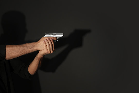Professional killer with gun on black background, closeup
