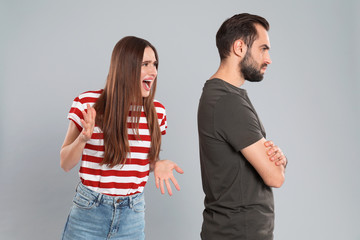 Woman shouting at her boyfriend on grey background. Relationship problems