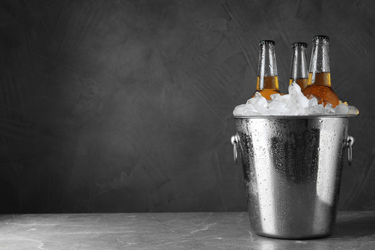 Beer in metal bucket with ice on marble table. Space for text