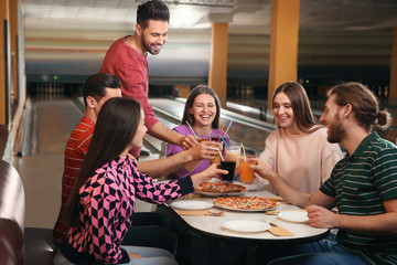Group of friends with drinks and pizza in bowling club