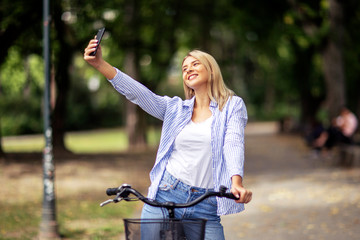 Blonde girl on bicycle taking selfie by mobile phone in the park