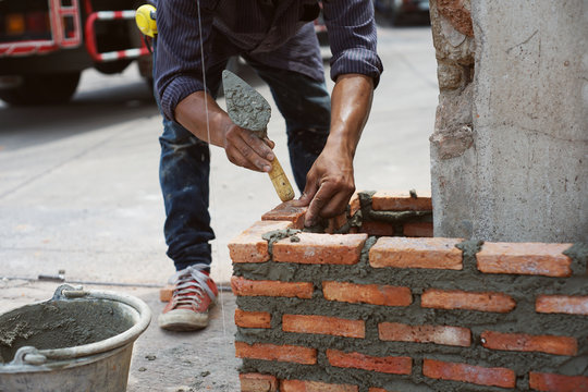 Construction worker laying bricks and building brick wall at exterior construction site .Detail of hand worker installing bricks .selective focus
