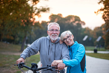 Fototapeta premium Older couple in park, he is with bicycle and she walk beside and talking