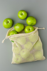 Green apples in a reusable cotton bag on a gray background.
