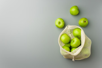 Green apples in a reusable white cotton bag on a gray background.