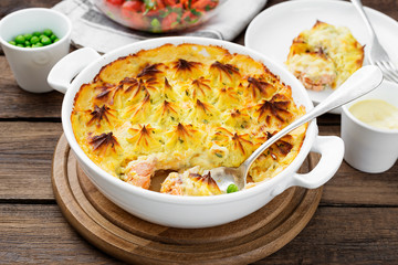 Fish pie with salmon, mashed potatoes, green peas and creamy sauce. on  wooden background.