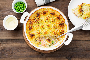 Fish pie with salmon, mashed potatoes, green peas and creamy sauce. on  wooden background.