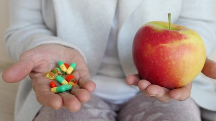 Senior Woman Holds An Apple In One Hand And A Handful Of Pills In The Other.