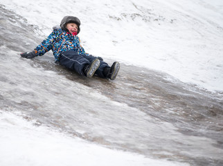 Fototapeta na wymiar Child rides on an ice slide. Cheerful boy in the winter.