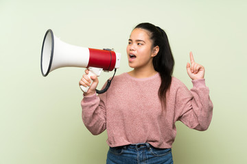 Young teenager Asian girl over isolated green background shouting through a megaphone