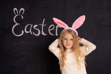 Cheerful provocative girl in the ears of a rabbit on the background of a black board with the inscription Easter in anticipation of the holiday.