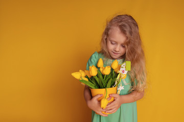 Cute cheerful girl in a green dress on a yellow background holds tulips in her hands and laughs merrily.