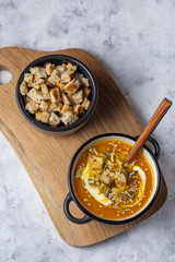 Pumpkin soup in a bowl with crackers and seeds and sour cream and a gray background top view