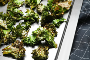 Tasty kale chips with seeds on baking sheet, closeup
