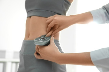 Nutritionist measuring woman's fat layer with caliper indoors, closeup