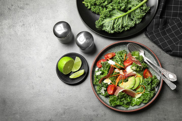 Delicious kale salad with prosciutto served on grey table, flat lay