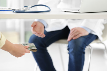 Obraz premium Patient giving bribe to doctor under table in clinic, closeup. Corrupted medicine