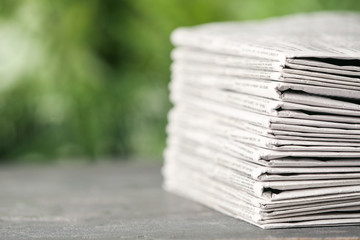 Stack of newspapers on grey table against blurred green background, space for text. Journalist's...