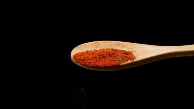 Slow motion of mixture of ground aromatic red spices falling down from wooden spoon against black background