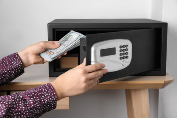 Woman putting money into steel safe with electronic lock, closeup