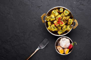 Aloo Methi in copper kadai, bowl at dark slate background. Aloo Methi is indian cuisine dish with Potato, Fenugreek and Spices. Indian Food. Copy space. Top view