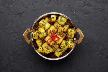 Aloo Methi in copper kadai, bowl at dark slate background. Aloo Methi is indian cuisine dish with Potato, Fenugreek and Spices. Indian Food. Copy space. Top view