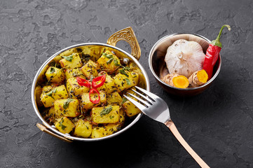 Aloo Methi in copper kadai, bowl at dark slate background. Aloo Methi is indian cuisine dish with Potato, Fenugreek and Spices. Indian Food.