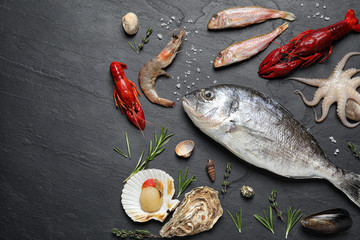 Fresh fish and different seafood on black table, flat lay