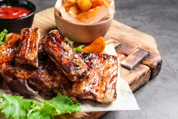 Delicious grilled ribs and garnish on grey table, closeup