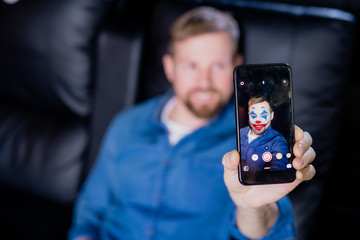 Young man with smartphone using multimedia application with face mask filter