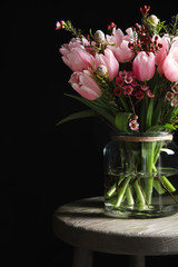 Beautiful bouquet with spring pink tulips on wooden table against black background
