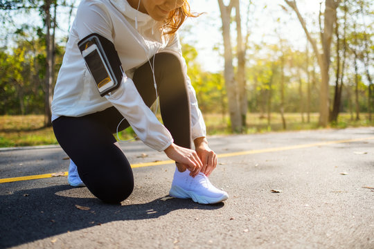 Closeup image of a woman runner tying shoelaces and getting ready for run in city park