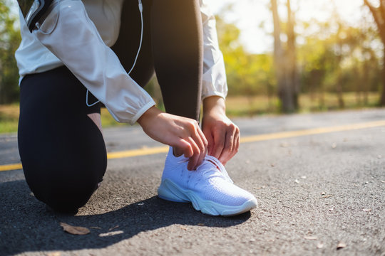 Closeup image of a woman runner tying shoelaces and getting ready for run in city park