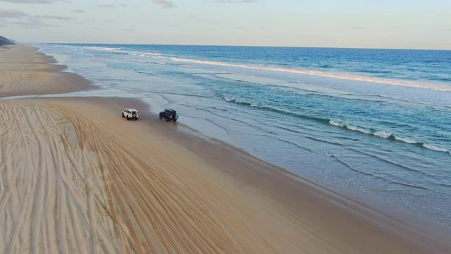 Stunning aerial drone footage of four-wheel drive off-road vehicles driving along the famous Seventy Five Mile Beach beach on the East Coast of Fraser Island, Queensland, Australia.