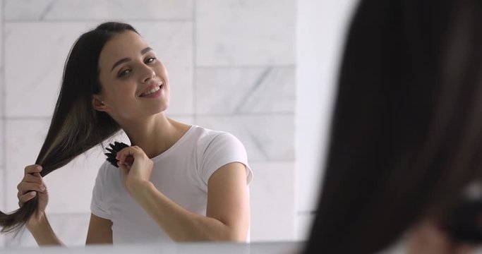 Attractive millennial lady combing long healthy straight hair.