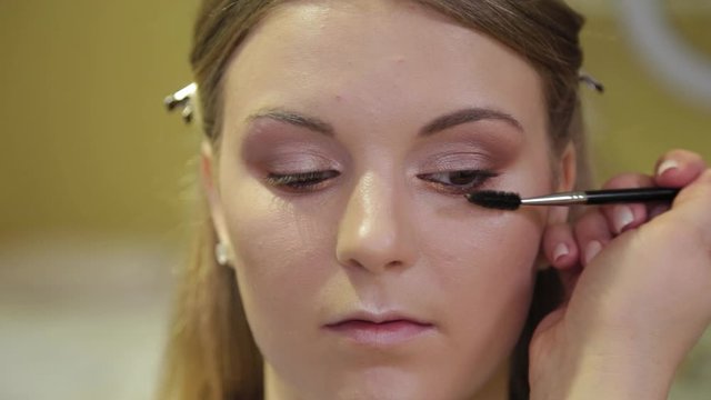 Professional makeup artist paints eyelashes to a client.