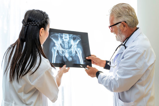 Medical professionals Caucasian senior man holding xray and conversation about patient with young doctor woman.