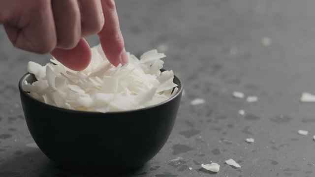 Slow motion man hand takes coconut chips from black bowl on terrazzo surface