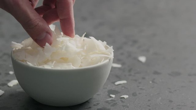 Slow motion man hand takes coconut chips from white bowl on terrazzo surface